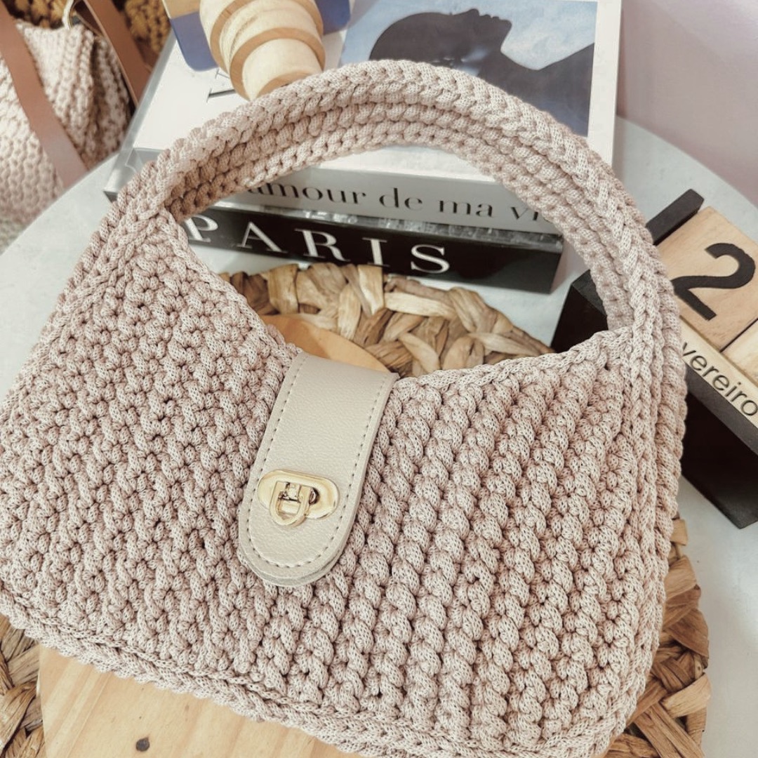 Detalhe da Bolsa Serena em flat lay com livros — fivela dourada elegante e ponto pipoca em destaque